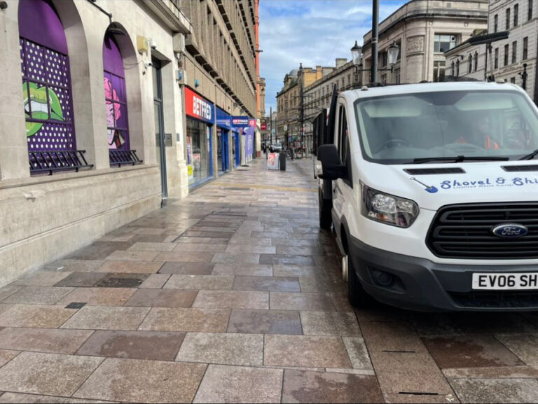 A van is parked on a sidewalk in front of a building.