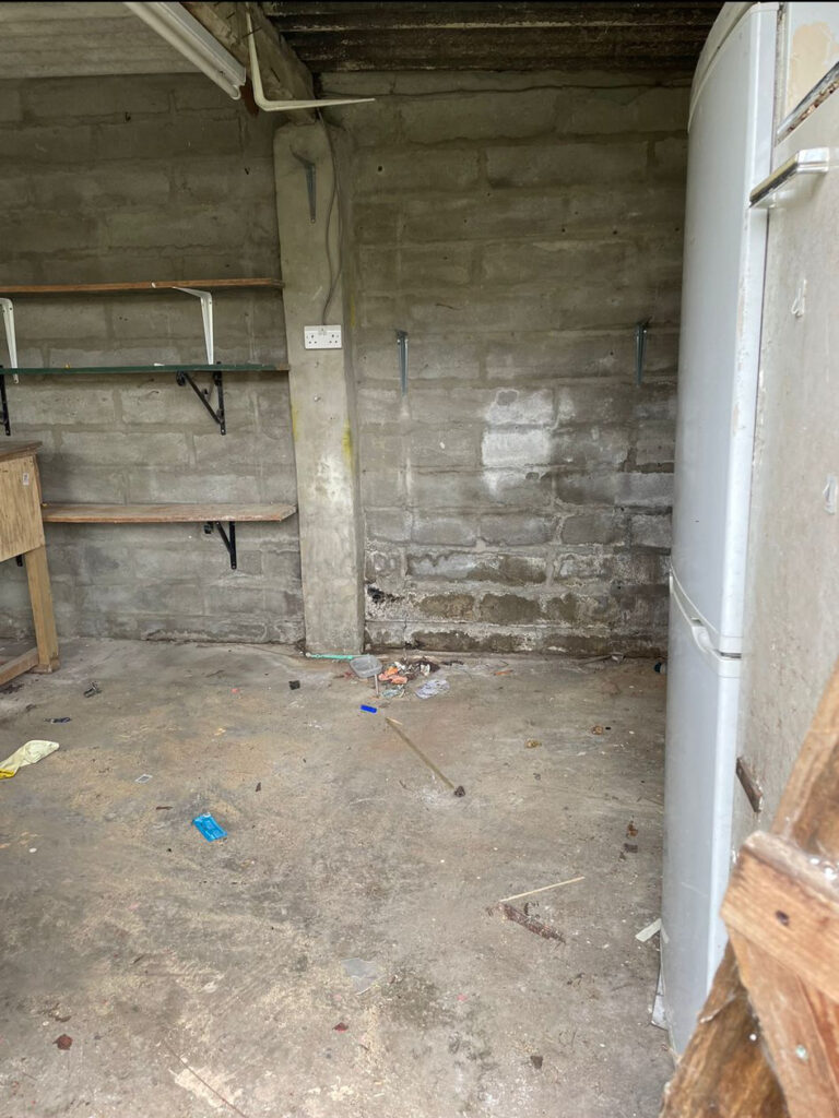 An empty room with a refrigerator and shelves.