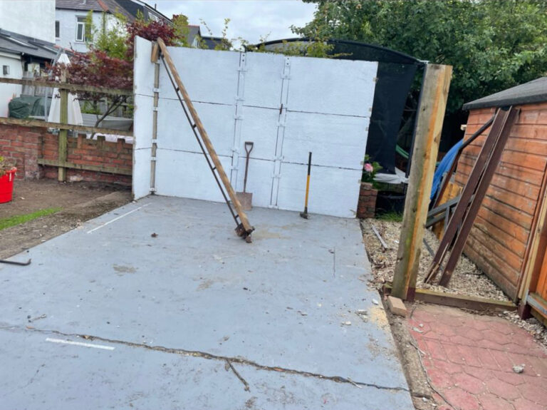 A backyard with a concrete wall and a shovel.