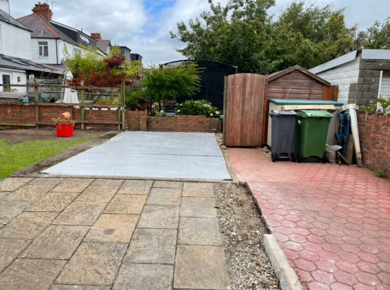 A backyard with a concrete patio and a trash can.